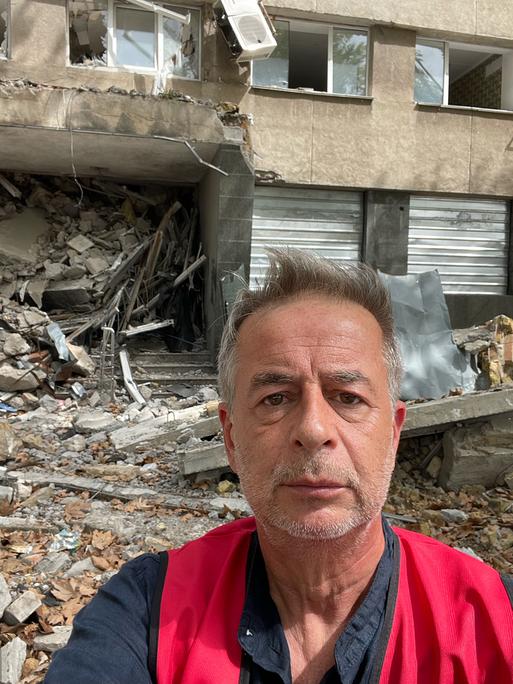 Andreas Tölke macht ein Selbstportrait vor einem zerstörten Haus in der Ukraine