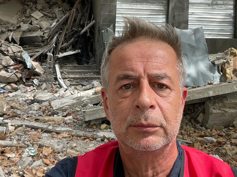 Andreas Tölke macht ein Selbstportrait vor einem zerstörten Haus in der Ukraine