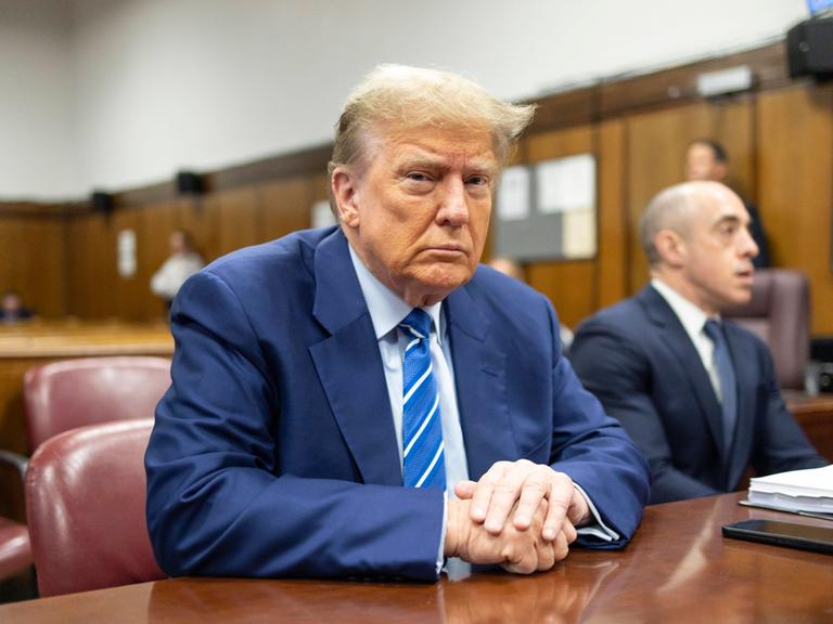 Donald Trump sitzt im Gericht an einem Tisch und blickt in die Kamera