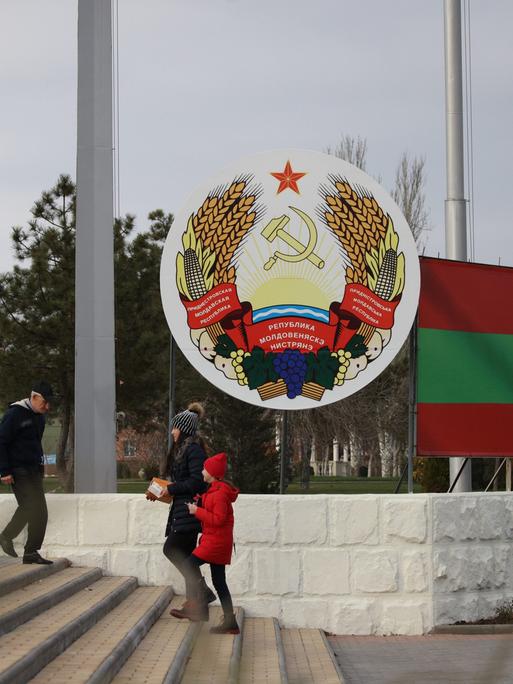 Menschen laufen am Wappen Transnistriens vorbei.