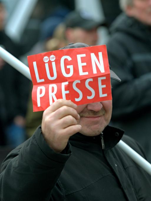 Ein Mann zeigt  dem Fotografen ein Schild mit der Aufschrift "Lügenpresse".