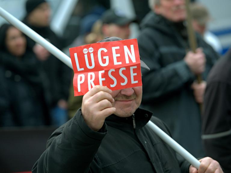 Ein Mann zeigt  dem Fotografen ein Schild mit der Aufschrift "Lügenpresse".