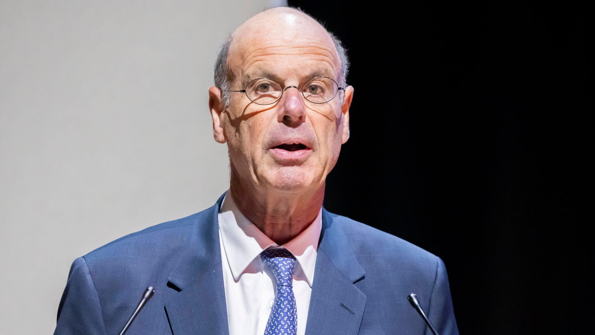 Der französische Finanzminister Eric Lombard spricht in zwei Mikrofone. Er trägt einen blauen Anzug, ein weißes Hemd und eine blaue Krawatte. Der französische Finanzminister Eric Lombard spricht in zwei Mikrofone. Er trägt einen blauen Anzug, ein weißes Hemd und eine blaue Krawatte.