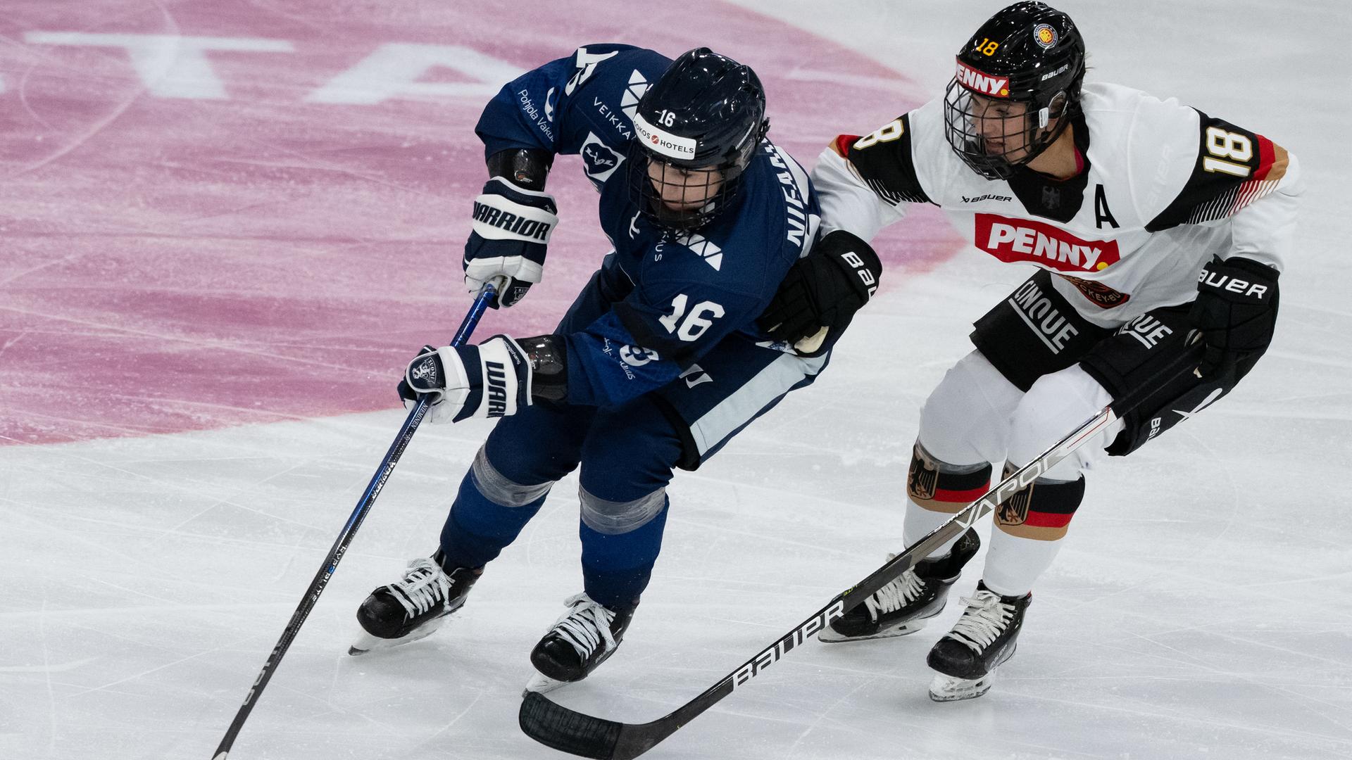 Die beiden gleiten nebeneinander über das Eis. Die Finnin im schwarzen Trikot führt den Puck. Karpf im weißen Trikot. Die beiden gleiten nebeneinander über das Eis. Die Finnin im schwarzen Trikot führt den Puck. Karpf im weißen Trikot.