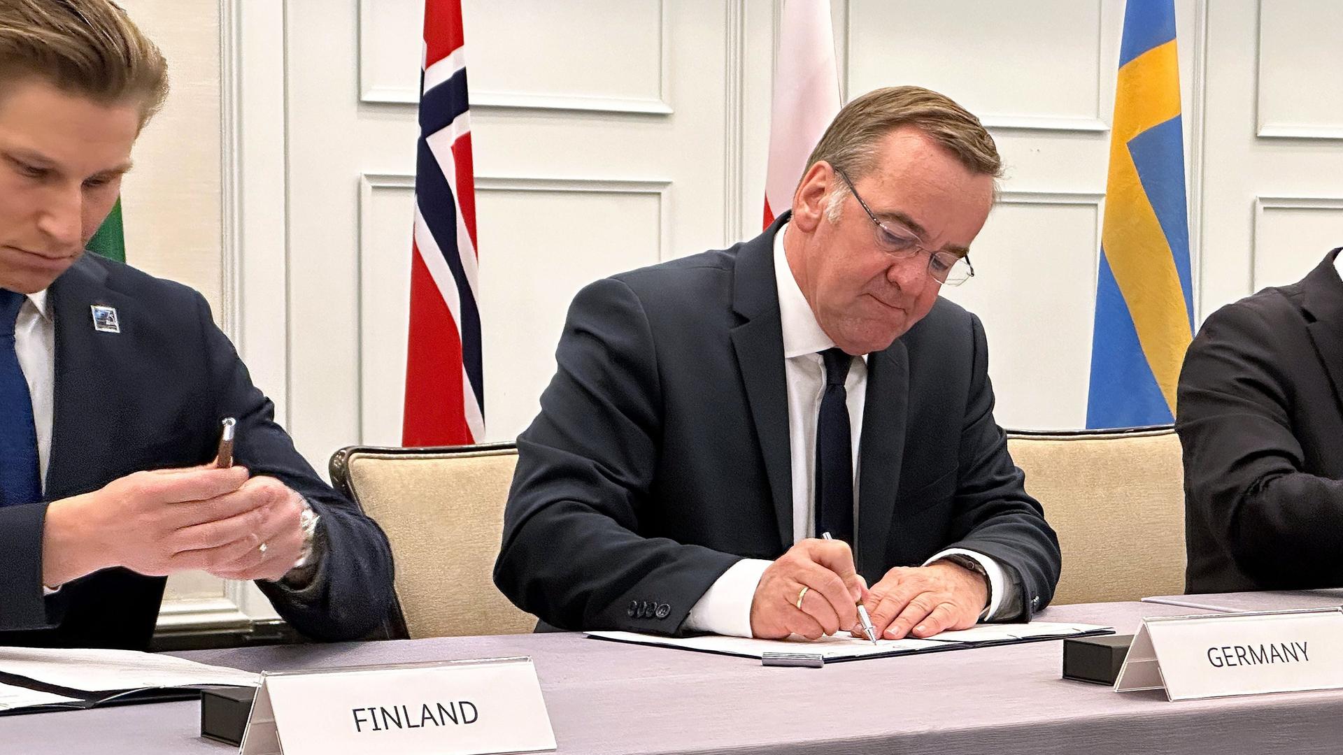 Pistorius und Häkkinen sitzen zusammen mit weiteren Vertretern an einem Tisch und unterzeichnen das Abkommen.