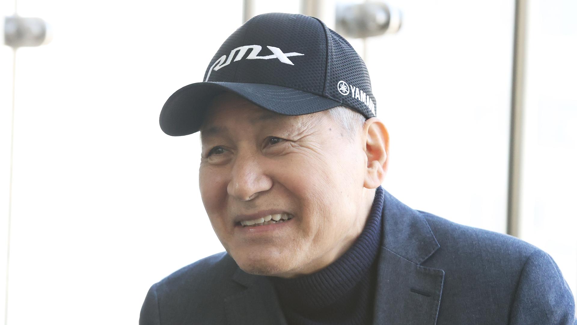 Ein Mann mit Rollkragenpullover, Jacket und Baseballmütze lächelt in die Kamera.