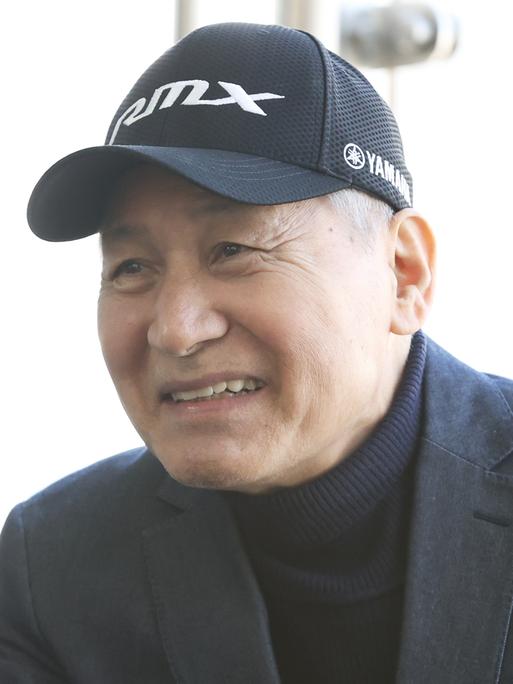 Ein Mann mit Rollkragenpullover, Jacket und Baseballmütze lächelt in die Kamera.