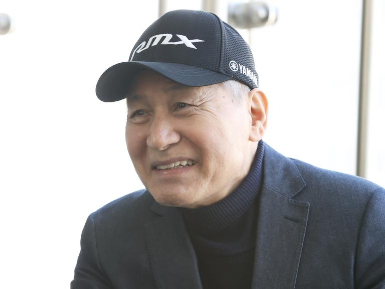 Ein Mann mit Rollkragenpullover, Jacket und Baseballmütze lächelt in die Kamera.