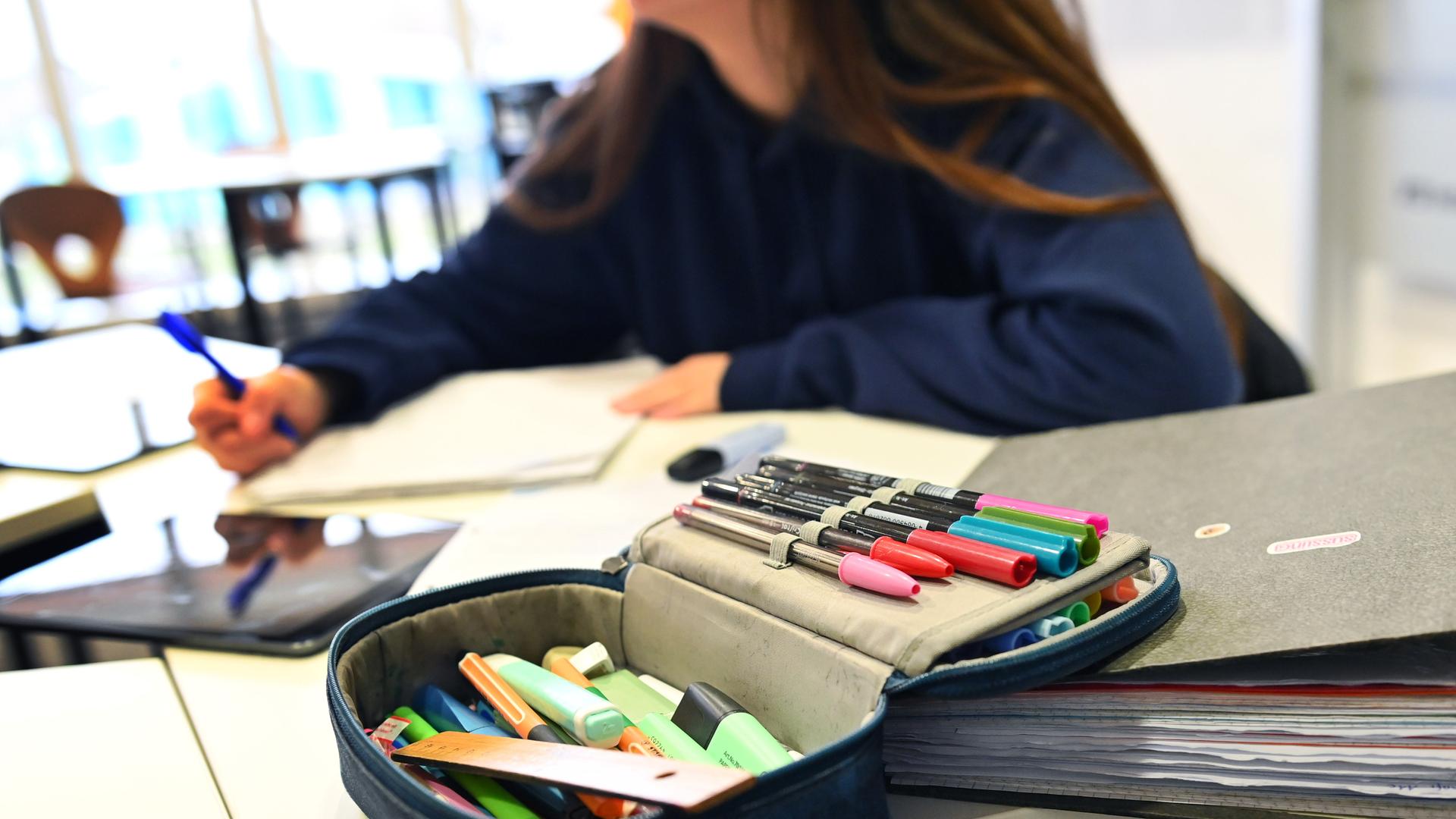 Eine Schülerin schreibt in ihrem Arbeitsheft, davor liegt ihre Federtasche.