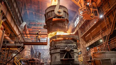 Ein Arbeiter im Schutzanzug beginnt mit dem Gießen von geschmolzenem Stahl im Stahlwerk in einer riesigen Produktionshalle.