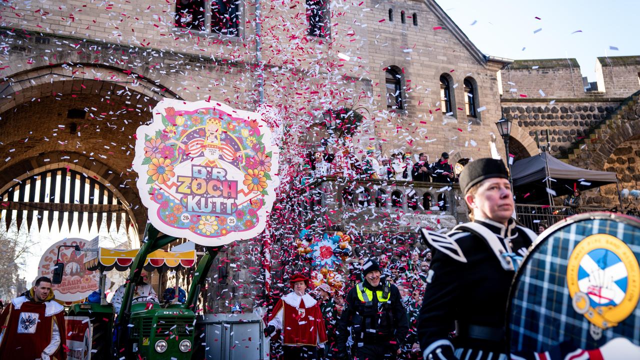 Der Beginn des Rosenmontagszugs in Köln. vor einem alten Stadttor fliegt viel Konfetti durch die Luft. Im Hintergrund ist ein Schild zu sehen mit der Aufschrift "D'r Zoch kütt", also "Der Zug kommt".