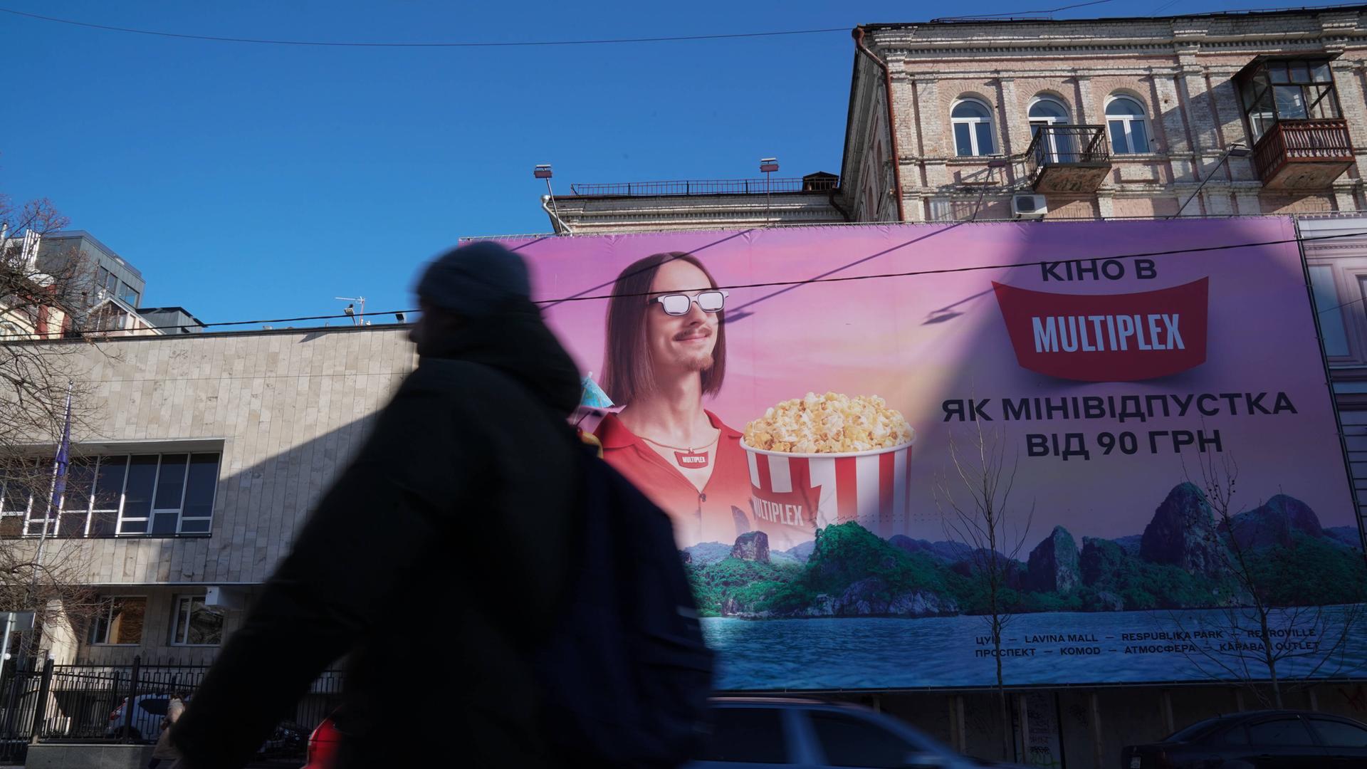 Auf einem Foto vom 4. Februar 2022 ist ein Passant zu sehen, der an einem großen Werbeplakat für ein Multiplex-Kino vorbeiläuft. Auf dem Plakat ist ein Mann mit Popcorn zu sehen.