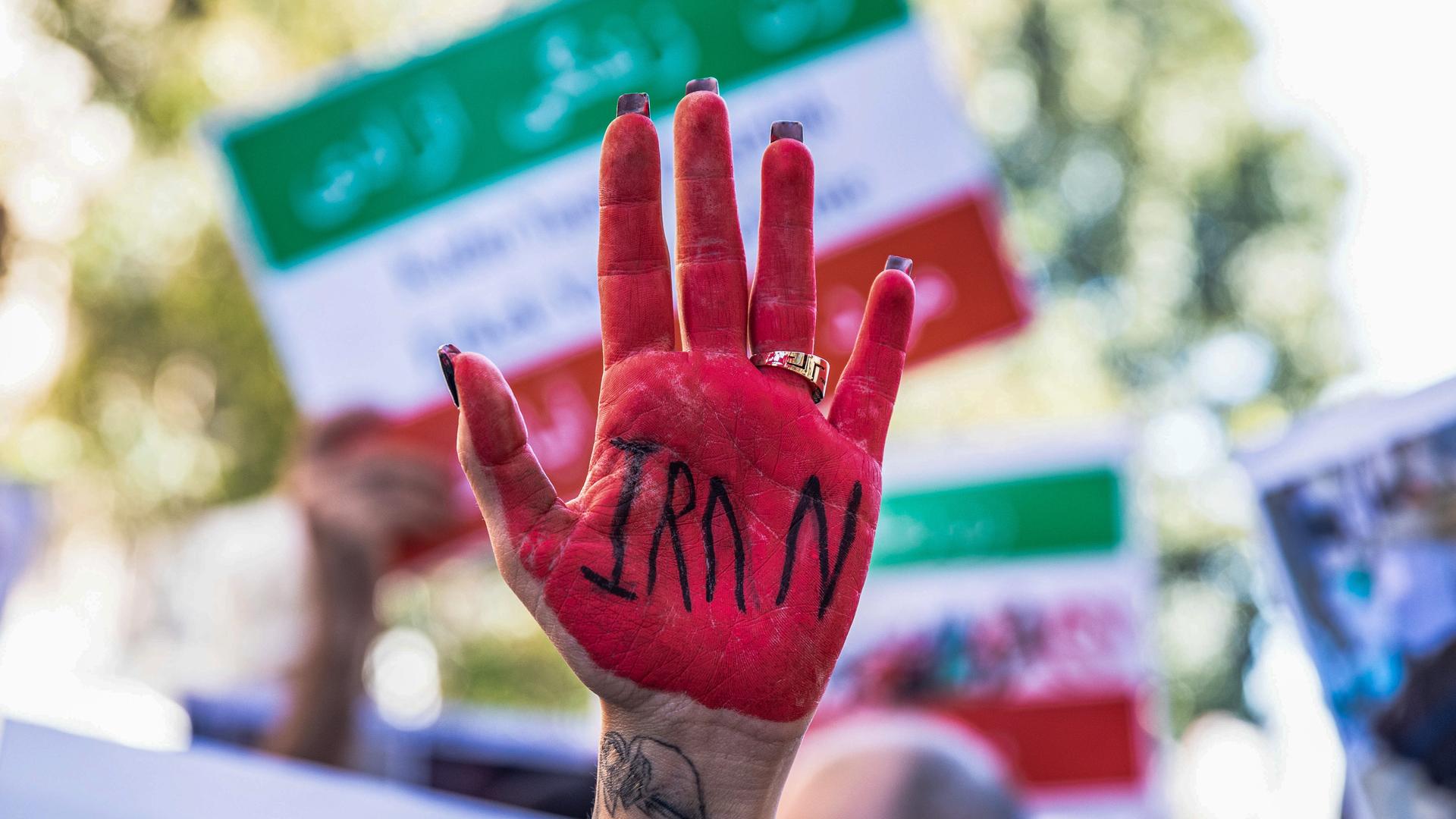 Eine Protestlerin hält eine in rot getränkte Hand mit der Aufschrift Iran in die Luft