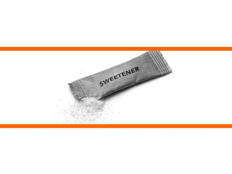 Schwarz-weißes Bild von einem Sachez Süßstoff vor weißem Hintergrund im mittleren Drittel des Bildes. Die beiden weißen Bilddrittel oben und unten sind mit orangenen Streifen abgetrennt.