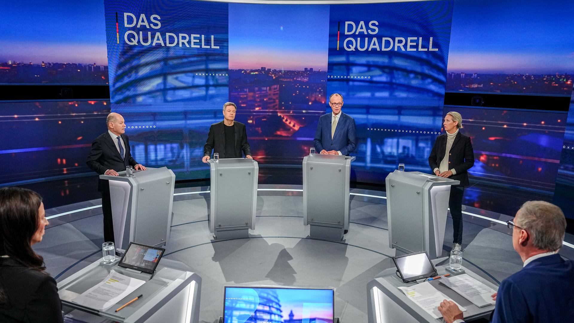 Olaf Scholz, Robert Habeck, Friedrich Merz und Alice Weidel stehen an Redepulten auf einer TV-Bühne, im Vordergund zu sehen sind die beiden Moderatoren Pinar Atalay und Günther Jauch.