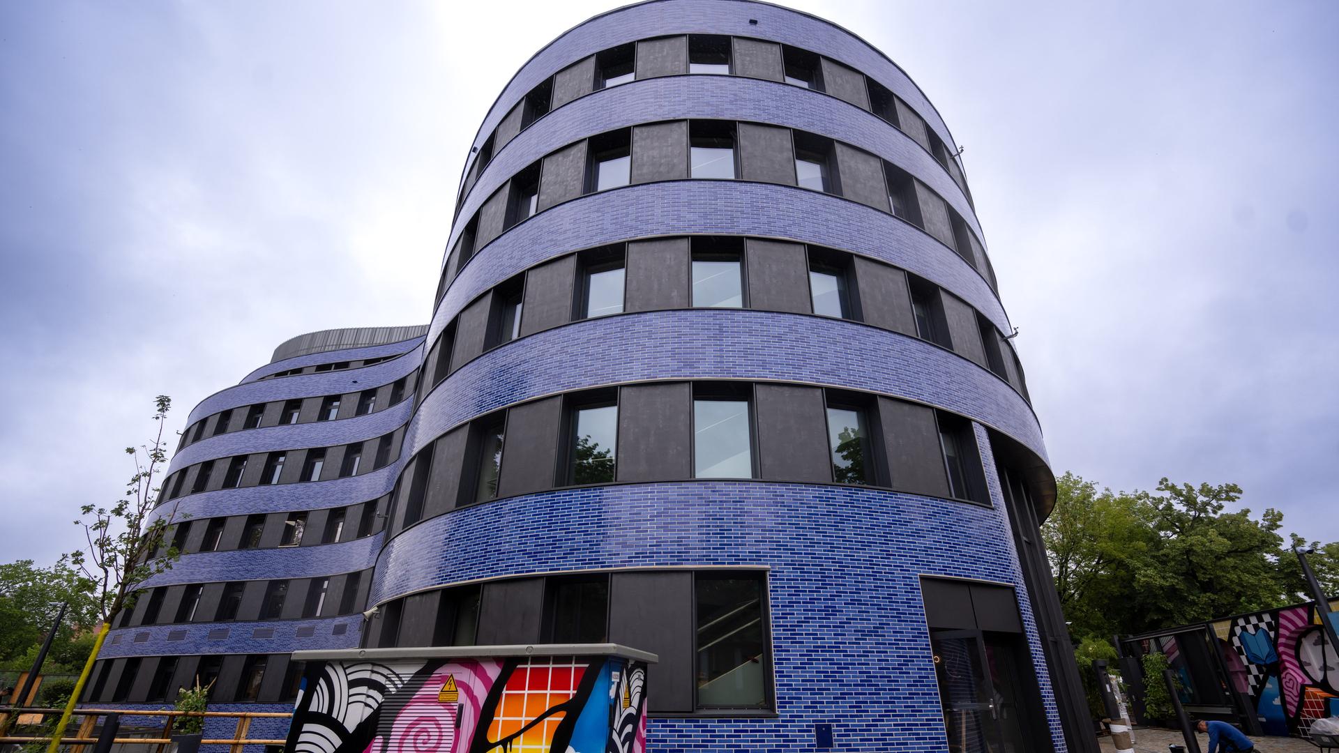 Das Foto zeigt das Gebäude von dem neuen jüdischen Campus in Berlin von außen. Im Vorder-Grund sieht man ein Grafitti, im Hinter-Grund Bäume.