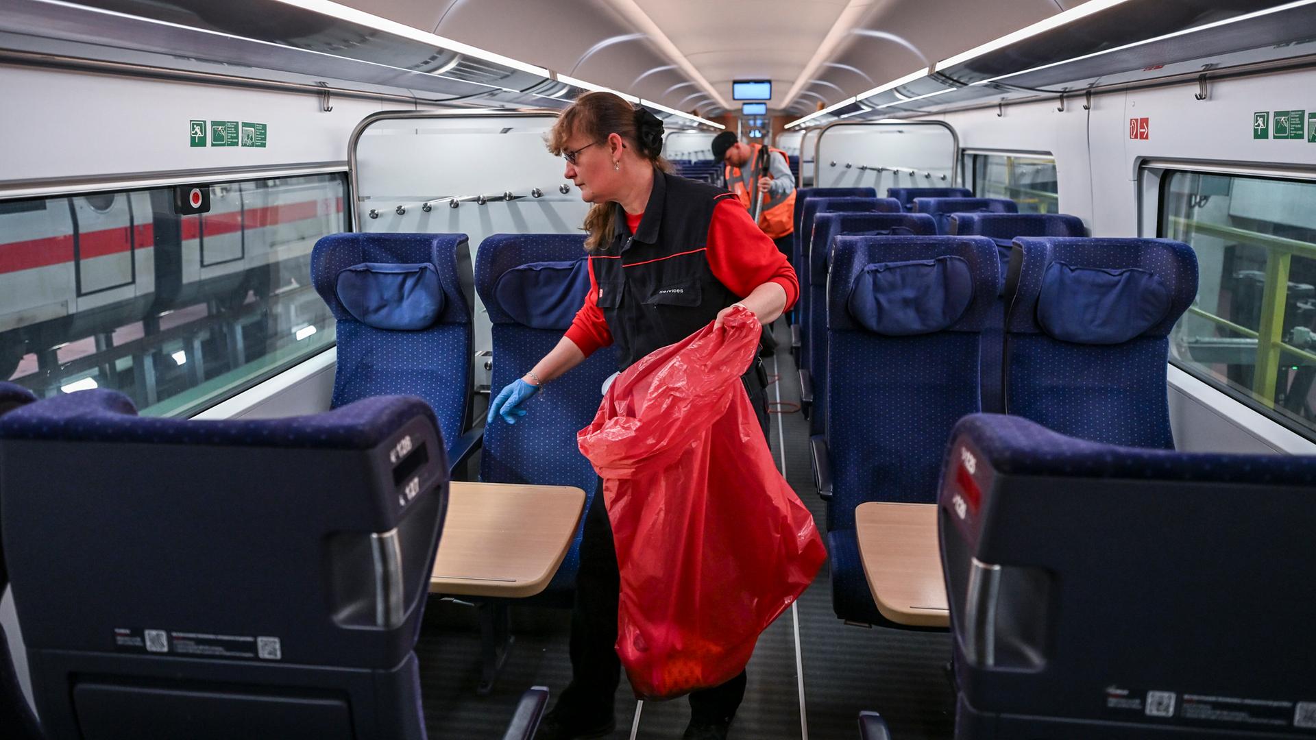 Eine Frau mit einem Müll-Sack in der Hand arbeitet in einem Abteil von einem ICE. Sie macht dort sauber.