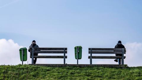 Zwei Personen sitzen bei blauem Himmel auf Sitzbänken auf einem Deich an der Weser in Bremerhaven.