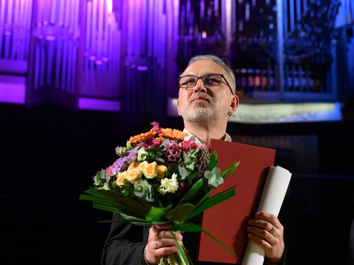 Bei der Auszeichnung mit dem Buchpreis zur Europäischen Verständigung steht der belarussische Schriftsteller Alhierd Bacharevič mit einem Blumenstrauß auf einer Bühne.