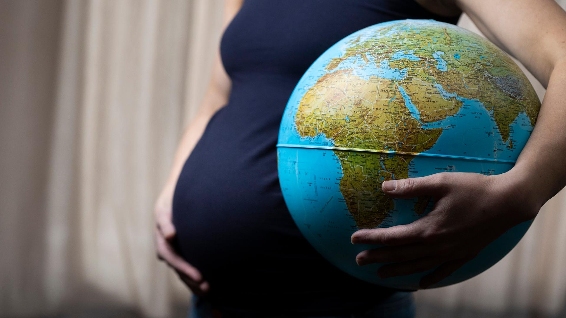 Schwangere Frau mit Globus unter dem Arm