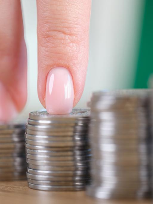 Die Finger einer Frau erklimmen eine Treppe, die aus Münzstapeln hergestellt wurde.