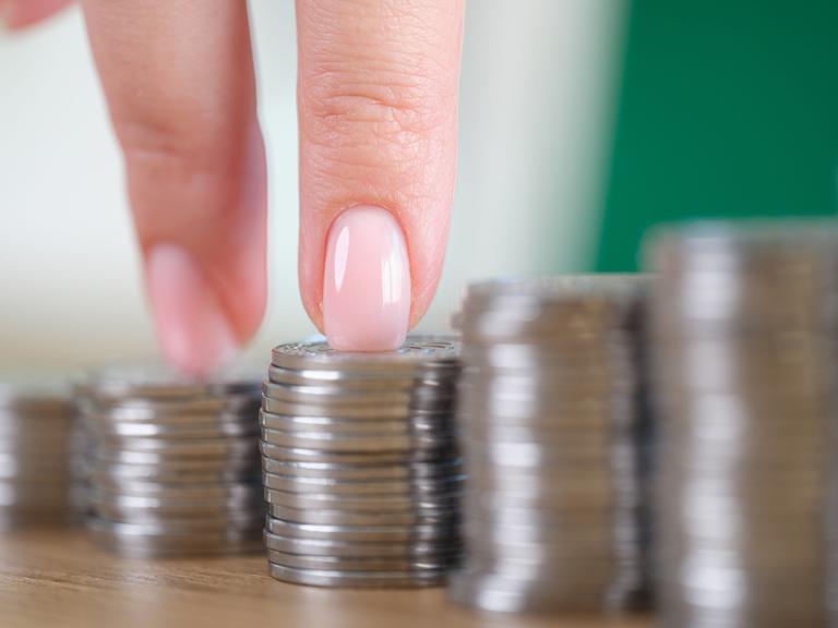 Die Finger einer Frau erklimmen eine Treppe, die aus Münzstapeln hergestellt wurde.