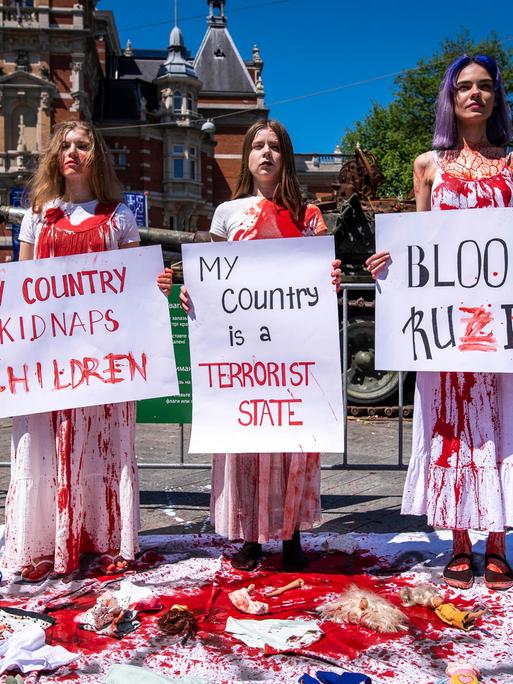 Anhängerinnen der Feminist Anti-War Resistance (FAS) demonstrieren gegen den russischen Angriffskrieg und halten mit roter Farbe verschmierte Protestschilder in der Hand.