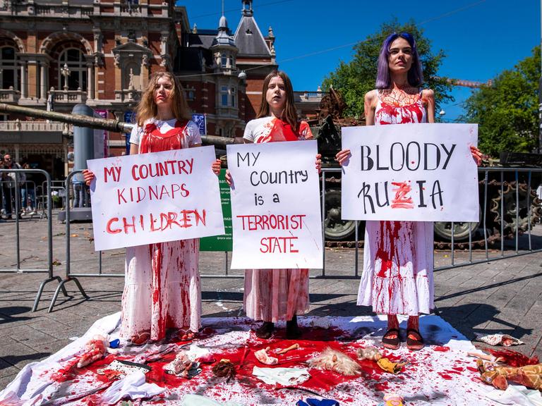 Anhängerinnen der Feminist Anti-War Resistance (FAS) demonstrieren gegen den russischen Angriffskrieg und halten mit roter Farbe verschmierte Protestschilder in der Hand.