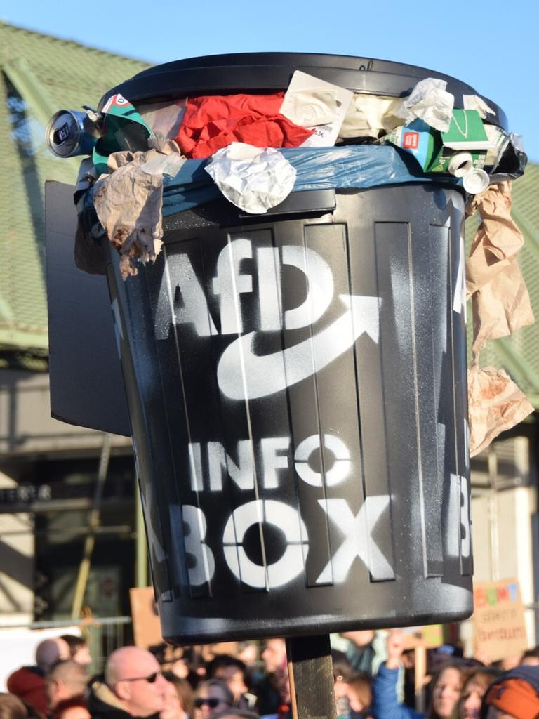 Auf einer Demonstration gegen Rechtsextremismus wird eine schwarze Tonne mit einem AfD-Logo hochgehalten. Die Tonne ist bis zum Rand gefüllt mit Müll.