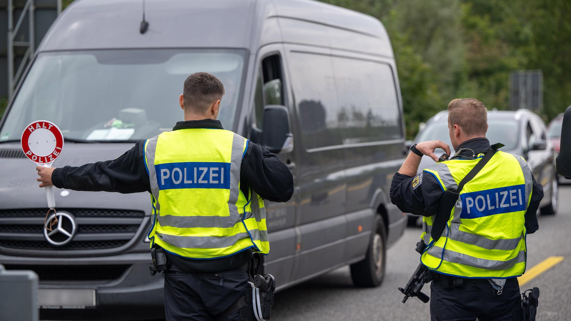 Polizisten kontrollieren Fahrzeuge an einer Autobahn.