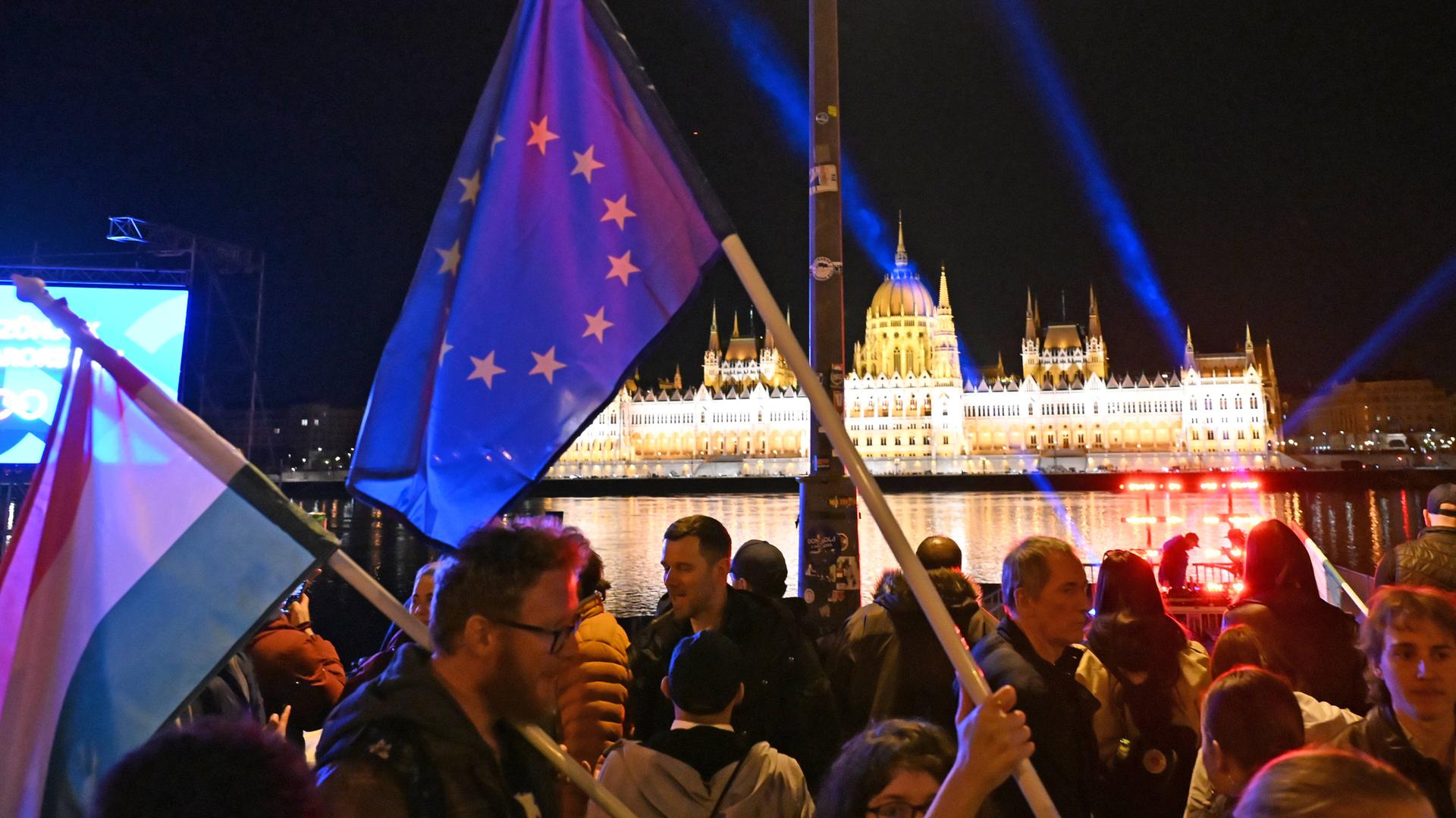 Menschen mit Ungarn- und EU-Flaggen in Budapest mit Blick auf die Donau. 