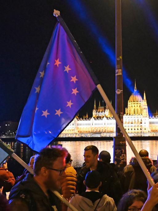 Menschen mit Ungarn- und EU-Flaggen in Budapest mit Blick auf die Donau. 