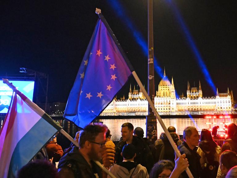 Menschen mit Ungarn- und EU-Flaggen in Budapest mit Blick auf die Donau. 