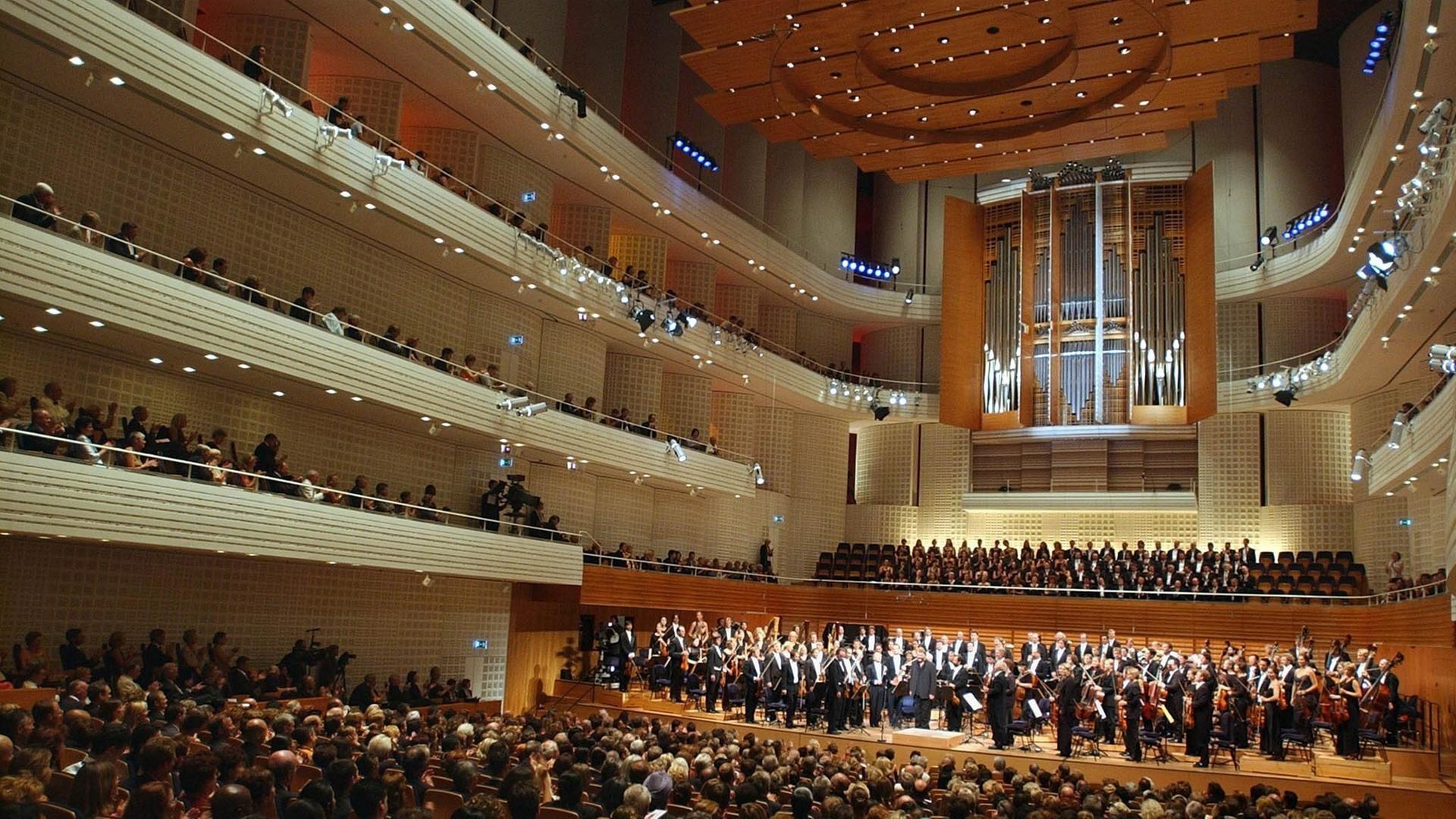 Ein voll besetzter Konzertsaal mit großer Orgel und beleuchteten Rängen. Das Orchester und der Chor stehen.