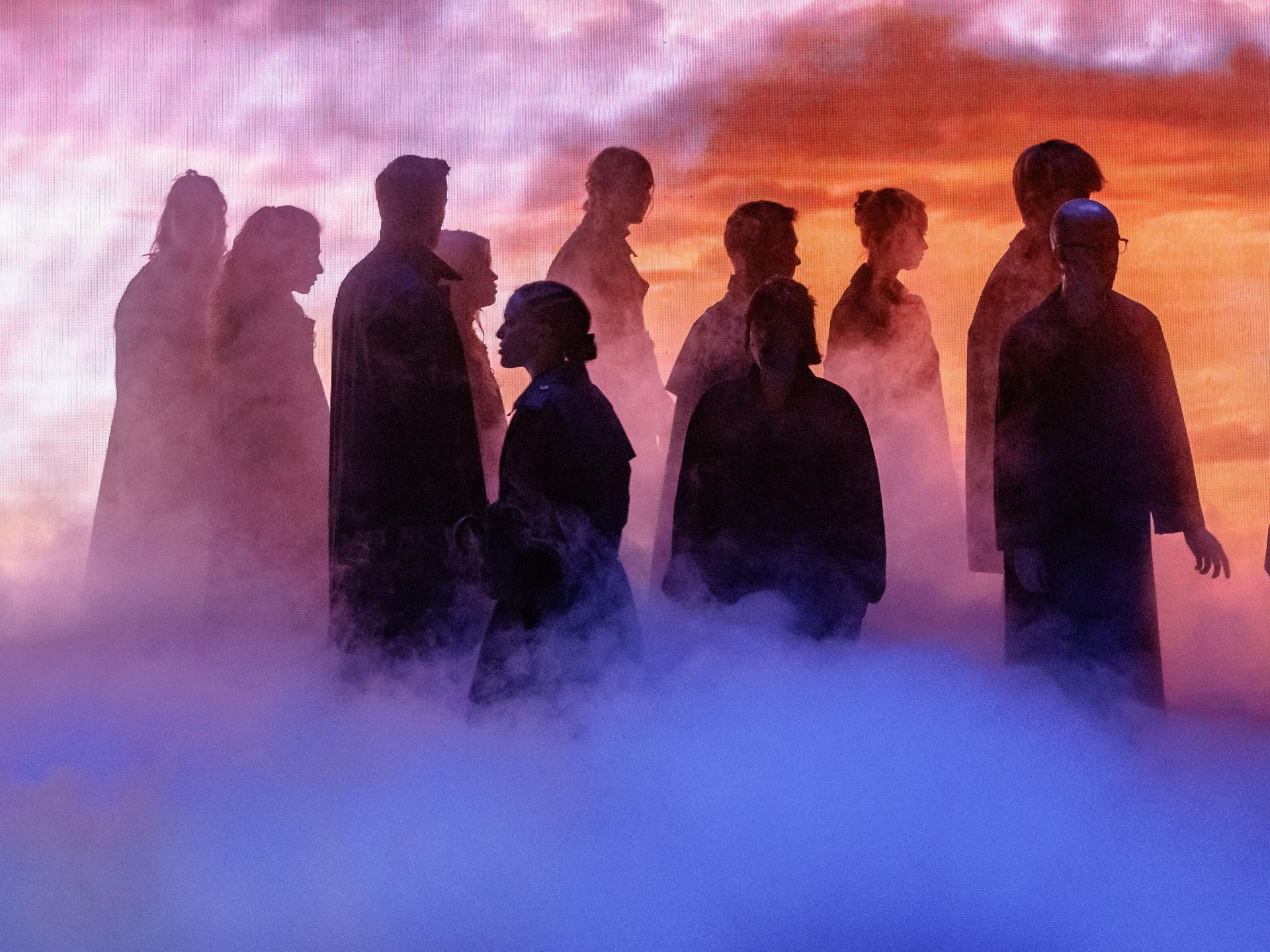 Szenenbild aus der Fotoprobe von "Barocco". Stimmungsvolle Bühnensituation mit einer Gruppe von Menschen, die nur als Silhouetten zu erkennen sind. 