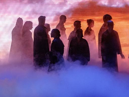 Szenenbild aus der Fotoprobe von "Barocco". Stimmungsvolle Bühnensituation mit einer Gruppe von Menschen, die nur als Silhouetten zu erkennen sind. 