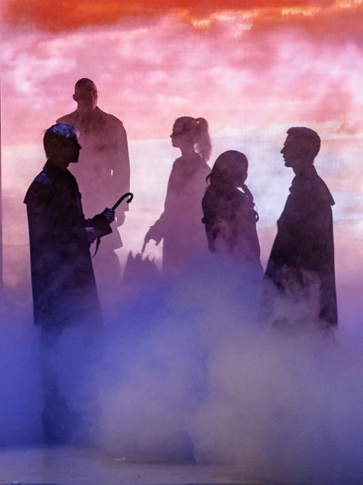 Szenenbild aus der Fotoprobe von "Barocco". Stimmungsvolle Bühnensituation mit einer Gruppe von Menschen, die nur als Silhouetten zu erkennen sind. 
