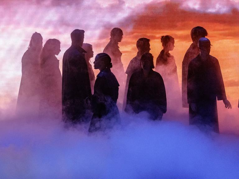 Szenenbild aus der Fotoprobe von "Barocco". Stimmungsvolle Bühnensituation mit einer Gruppe von Menschen, die nur als Silhouetten zu erkennen sind. 