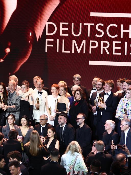 Die Personen stehen dicht beieinander zum Gruppenfoto in mehreren Reihen. Über Ihnen ist in großen Buchstaben "Deutscher Filmpreis" zu lesen