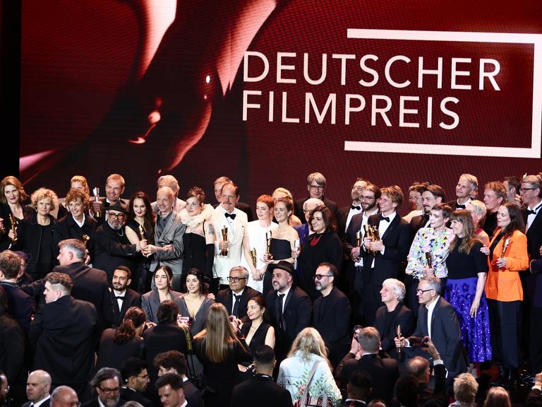 Die Personen stehen dicht beieinander zum Gruppenfoto in mehreren Reihen. Über Ihnen ist in großen Buchstaben "Deutscher Filmpreis" zu lesen