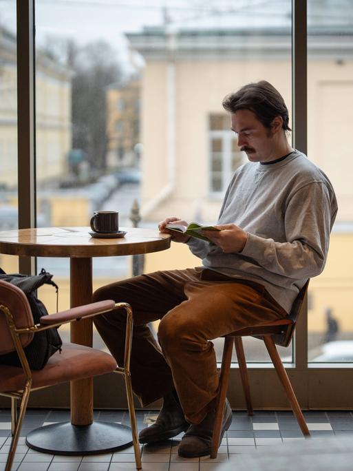 Ein Mann sitzt in einem Café und liest nachdenklich ein Buch Ein Mann sitzt in einem Café und liest nachdenklich ein Buch
