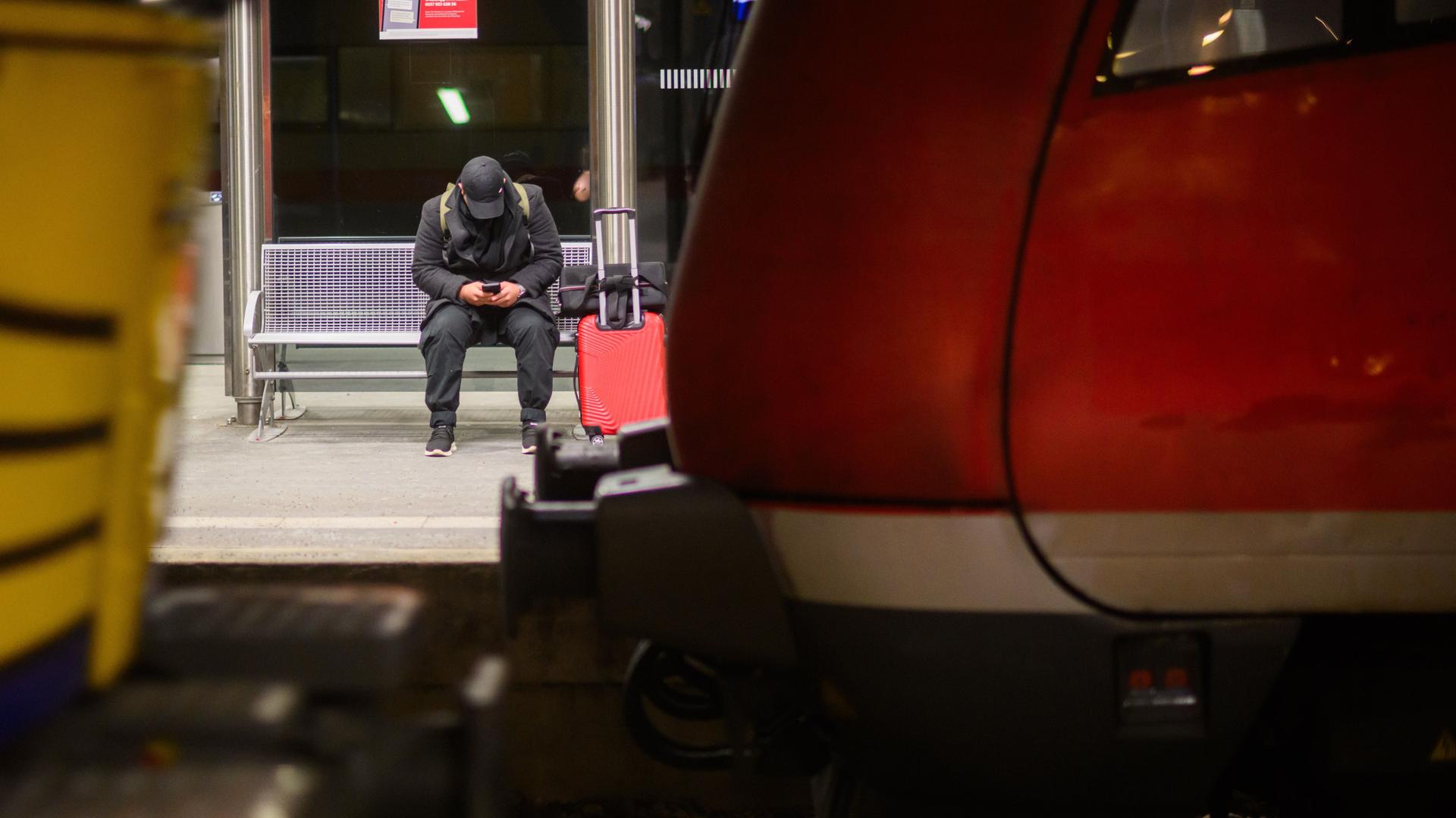 Ein Mann wartet mit Koffer an einem Gleis im Hauptbahnhof Hannover. 