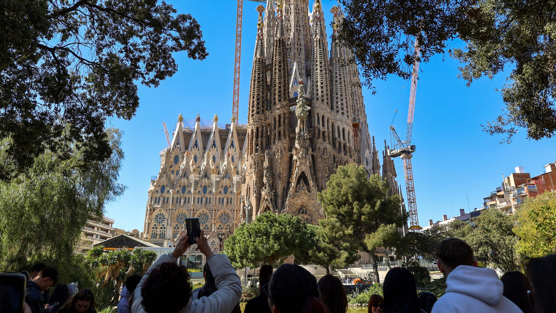 Blick auf die weltberühmte Basilika 'Sagrada Familia' von Gaudi in Barcelona, eine Touristengruppe steht in der Nähe und macht Fotos davon.