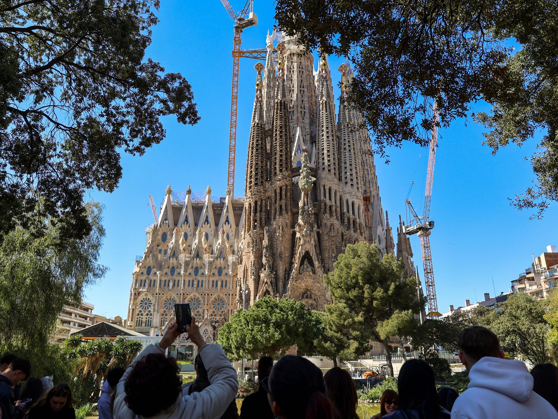 Blick auf die weltberühmte Basilika 'Sagrada Familia' von Gaudi in Barcelona, eine Touristengruppe steht in der Nähe und macht Fotos davon.