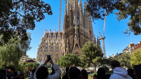 Blick auf die weltberühmte Basilika 'Sagrada Familia' von Gaudi in Barcelona, eine Touristengruppe steht in der Nähe und macht Fotos davon.