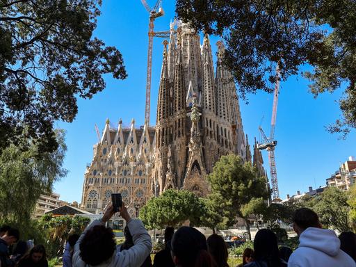 Blick auf die weltberühmte Basilika 'Sagrada Familia' von Gaudi in Barcelona, eine Touristengruppe steht in der Nähe und macht Fotos davon.