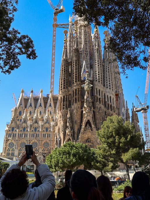 Blick auf die weltberühmte Basilika 'Sagrada Familia' von Gaudi in Barcelona, eine Touristengruppe steht in der Nähe und macht Fotos davon.