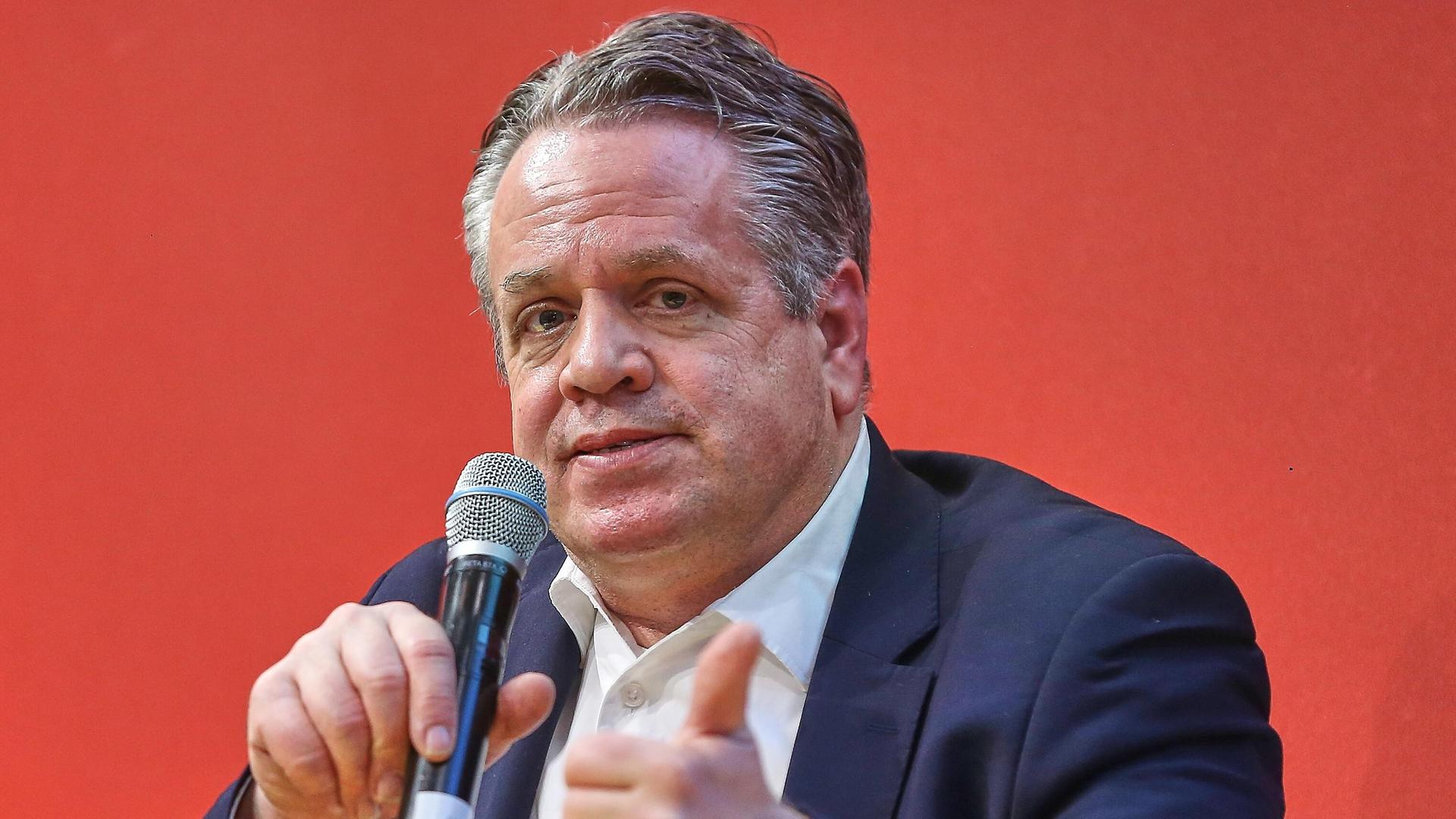 Marcus Bensmann sitzt bei der Leipziger Buchmesse vor einem roten Hintergrund mit einem Mikrofon in der Hand auf einem Podium.