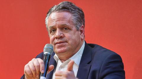 Marcus Bensmann sitzt bei der Leipziger Buchmesse vor einem roten Hintergrund mit einem Mikrofon in der Hand auf einem Podium.