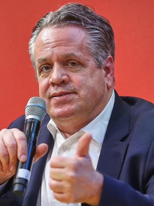 Marcus Bensmann sitzt bei der Leipziger Buchmesse vor einem roten Hintergrund mit einem Mikrofon in der Hand auf einem Podium.